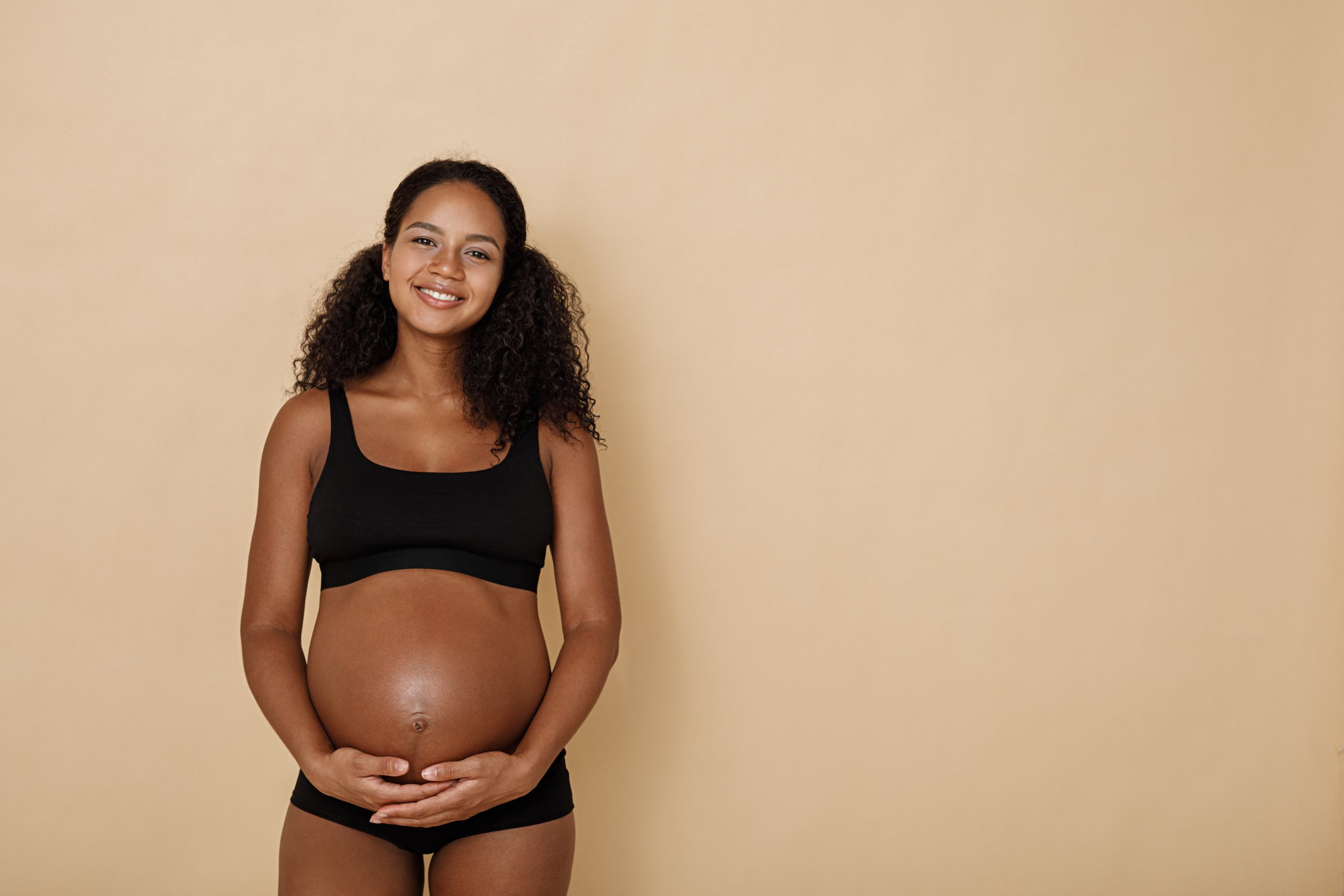 Pregnant Woman Wearing Black Lingerie on Beige Background